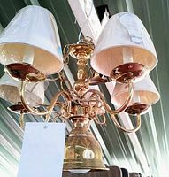 Angle view of polished brass chandelier showing five candle-arms with white mini shades and lower bulb fixture.