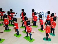 Multiple red-uniform British Guardsmen toy soldiers arranged on a surface for display, showing various poses including standing and aiming rifles.