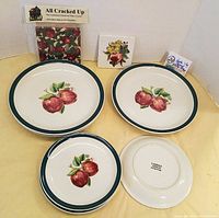 Overview of six apple casual plates with red apple motifs (two large, four smaller) and one packaged apple-themed electrical outlet cover.