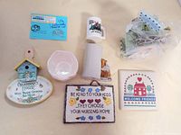 Lot of small vintage collectibles with mugs, bird houses, plaques, and ceramic bowl arranged on a pale surface