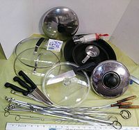 Lot of vintage cooking items including two black frying pans, three glass lids, metal vent cover, cutting knives, measuring cup, skewers, and a manual beater.