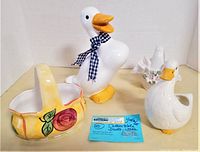 Full view of four ceramic items: white duck with checkered ribbon, white goose, yellow basket, and white vase with flower decoration, with seller note in front