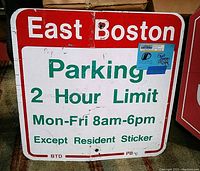 Front side of a vintage East Boston parking sign showing red, white, and green colors. Text states a 2 hour parking limit, with timing and resident sticker exception. Sign shows wear and paint chipping, with a bent shape.