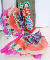 Vintage fabric butterfly dragonfly kite body upright with bright, colorful detached wings and attached string spread around on floor against a fabric backdrop