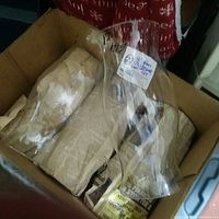 Five vintage clear glass chimneys for hurricane lamps shown inside a cardboard box with newspaper.