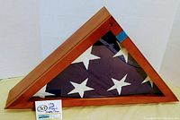 Triangular wooden flag display case with folded American flag visible through clear glass front, showing white stars on blue field.