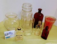 Lot of eight vintage glass bottles and vase displayed on yellow cloth background. Items include clear and brown glass bottles and one clear glass vase. Various shapes and sizes.