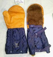 Pair of vintage US Air Force air crew mittens showing leather palm and thumb, navy blue nylon cuffs with U.S. Air Force embroidered logos, and attached straps and snaps for wrist adjustment.