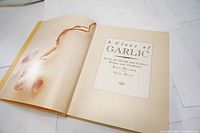Open cookbook page showing garlic illustration and title page with book title and authors.