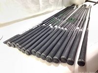 Photo showing 15 golf shafts laid out with PING logos visible on shafts and black Golf Pride grips on ends.