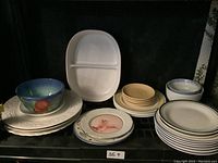 Overview of assorted plates, bowls, cups, and serving platter including the blue bowl with pomegranate design and stacked white plates.