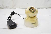 Front view of the Wanscam IP surveillance camera with power adapter connected by a wire, camera lens surrounded by infrared LEDs.