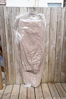 Curtain panels folded and sealed in plastic packaging showing soft textured brown beige fabric and rod pocket at top, hanging on a wooden fence for display.