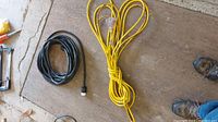 Two heavy duty electrical cords on floor; one black, one long yellow cord wrapped and tied.
