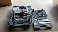 Overview of two open tool kits showing various hand tools, socket wrenches, pliers, hammers, and bits in molded plastic cases.