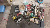 Wide overview of all drill bits, Allen keys, screwdriver handles, and other hand tools scattered on a dark surface.