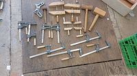 Overview photo showing the full assortment of wooden mallets and various clamps including bar clamps and C-clamps laid out on a wooden surface.