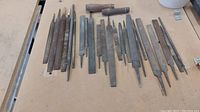 Full view of assorted metal files laid out on a table, showing variation in length and thickness, some files with wooden handles and others without.