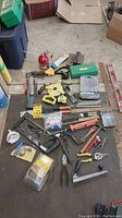 Wide view of assorted tools including hand screwdrivers, pliers, clamps, and hole saw kit in green case spread out on floor