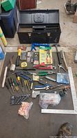 Full lot layout with metal toolbox and assorted hand tools including hammers, screwdrivers, pliers, measuring tape, utility knife, and small parts laid out on floor.