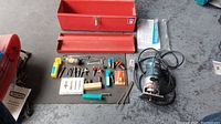 Layout of Bosch Colt router and accessories including red toolbox and assorted bits.
