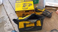 Yellow and black DeWalt random orbit sander with power cord, original yellow DeWalt sander box, and a black and yellow DeWalt carrying bag placed on a wooden floor.