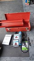 Photo of open red steel toolbox with removable tray, and items including blue Mastercraft multi-tool, sanding sheets, tool blades, and instruction manual arranged on floor.