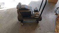 Side view of the Mastercraft branded portable air compressor showing wheels and motor unit on top of the tank