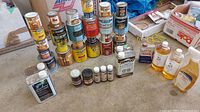 Photo showing multiple stacked metal cans of various Minwax wood stains and varnishes, with additional wood finishing oils and cleaners in front.