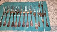 Full display of 15 forks on a blue cloth, showing the 10 larger and 5 smaller forks.