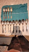 Photo showing all 13 spoons, 9 large soupspoons and 4 smaller bouillon spoons, arranged on a teal fabric holder.