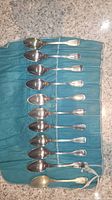 Set of 11 silver teaspoons with Chinon pattern laid out on blue fabric roll on granite countertop.