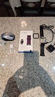 Fitbit Blaze smartwatch with black band, charging cable, black face case, purple replacement band in box, wireless mouse, and Samsung USB converter all laid out on counter.