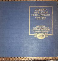 Front cover of a blue textile-covered record album labeled 'Gilbert-Sullivan Pirates of Penzance (Comic Opera in Two Acts)' with gold embossed lettering and Victor Records logo.