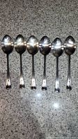 Six large silver spoons laid flat showing bowls and handles.