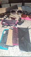 Overview of sunglasses, reading glasses, and several cases and pouches arranged on a countertop.