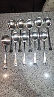 Set of 10 silver soup spoons with rounded bowls and Art Deco style handles on a granite countertop.