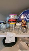 Multiple empty glass jars and tins, predominantly clear jars with lids, a red Quality Street tin, and an Atlantis Butter Cookies tin in the background.