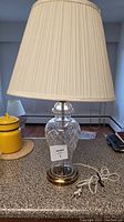 Full view of the vintage lamp showing the pleated cream lampshade, cut crystal body, brass base, and electrical cord.
