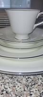 Stacked place setting showing teacup, saucer, salad and bread plates with silver rims.