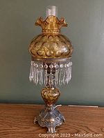 Full view of amber glass parlour lamp with ruffled shade, crystal prism fringe, metal base