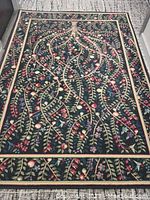 Full view of apple tree design polypropylene area rug with branches, apples, and flowers on dark background.