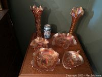 Overview of two tall slim carnival glass vases and four carnival glass dishes arranged on a wooden surface with a soda can for scale.