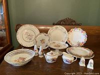Full overview of the entire set displayed on a bench showing all items with floral designs including plates, cake stand, sugar bowl, creamer, salt and pepper shakers, and a lattice bowl.