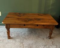Front view of rustic solid wood coffee table with tabletop, drawer, and turned legs visible.
