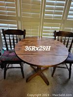 Photo of the stained oak drop leaf table with two chairs behind it, showing dimensions 36R x 29H written on the table surface.