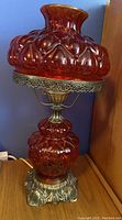 Full view of vintage red glass lamp with ornate brass base and top shade against blue wall