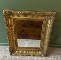 Front view of the entire mirror showing gold-tone, carved wood frame and bevelled glass.