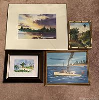 Four framed artworks arranged on carpet showing variety of landscapes and seascapes