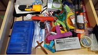 Drawer with assorted household and repair items including clips, knife, screwdrivers, adapters, wires, batteries, bulbs, and tape.